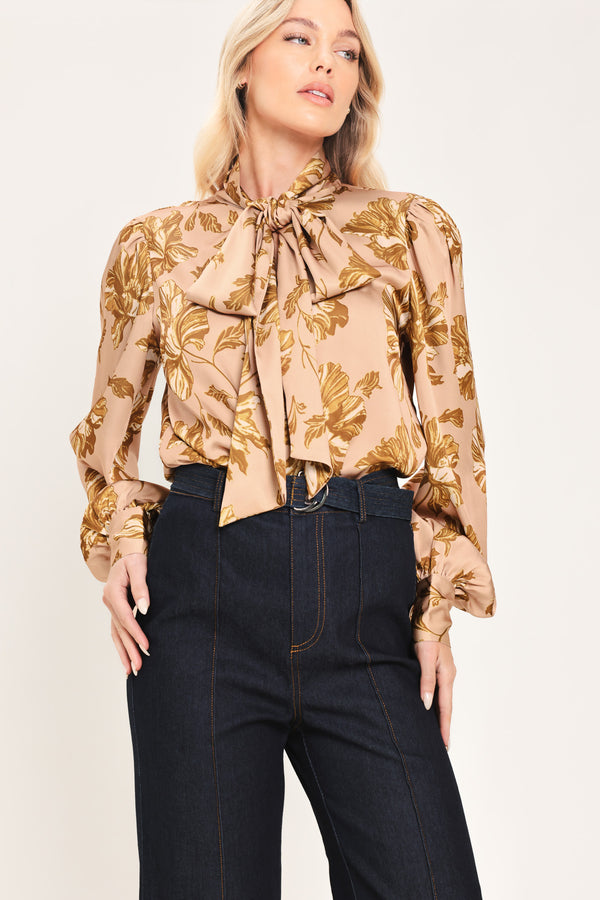 Woman wearing a long sleeve mauve top with a beige floral print and bow around the neck | Flying Tomato